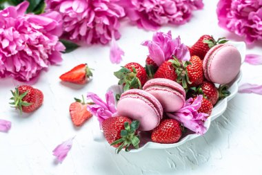 Pink peony with macarons and sweet strawberry on a white background. Small French cakes Macarons with fruit. top view.