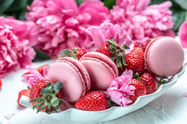 French cakes Macarons with fruit and pink peonies on white background. French delicate dessert for Breakfast in the morning light.