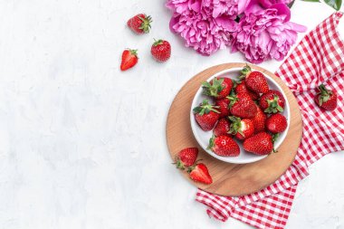Delicious fresh red strawberries with Pink peony flowers. on a white kitchen table, place for text, top view,
