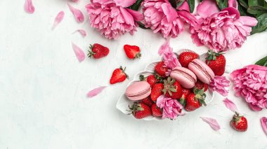 Closeup colorful macarons, Pink peony rose flower and sweet strawberry. Small French cakes with fruit. Long banner format. top view.