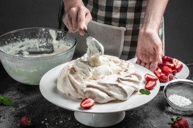 Lezzetli kremalı pasta dekore eden kadın fırıncı, bitmemiş pavlova pastası. Krem şantili ve çilekli krema. Mutfak, fırın, yemek ve insan konsepti.