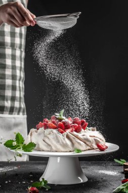 Lezzetli ev yapımı Pavlova pastası taze çilek ve krem şantili. Şefin elleri toz bulutu gibi dondurucu bir hareketle havada uçuyor. Mutfak, yemek pişirme, fırın konsepti,