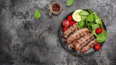 Domuz pastırmasına sarılı ızgara sosis, ıspanak, avokado ve vişneli domates. Chevapchichi ya da Kofta kebabı, diyet öğle yemeği konsepti. Keto paleo diyet menüsü,