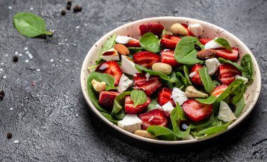 Çilekli vejetaryen salatası, ıspanak yaprağı, fındık ve peynir, balzamik sirke. Detoks ve sağlıklı yiyecek kasesi konsepti.