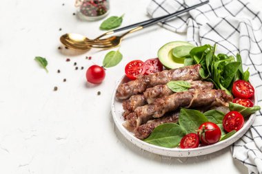 Domuz pastırmasına sarılı ızgara sosis, ıspanak, avokado ve vişneli domates. Chevapchichi ya da Kofta kebabı, diyet öğle yemeği konsepti. Keto paleo diyet menüsü,