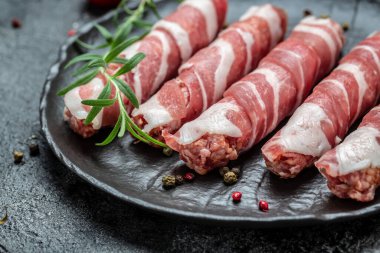 Domuz pastırmasına sarılı kıyma, dökme demir tabakta. Chevapchichi veya Kofta kebabı. Domuz pastırmasına sarılmış soğan ve baharatlı kıymalı çiğ sosis ya da domuz eti..