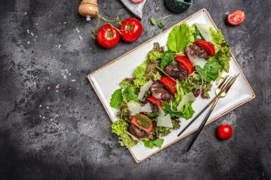 Tavuk ciğerli sıcak salata, mantar, salata yaprakları, parmesan peyniri ve tabakta vişneli domates. Sağlıklı yemek, afiş, menü, metin için tarif yeri, üst görünüm.