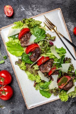 Kızarmış tavuk ciğeri salatası, salata yaprakları, parmesan peyniri ve vişneli domates. Sağlıklı yiyecekler. Beslenme menüsü. dikey görüntü. Üst Manzara. metin için yer.