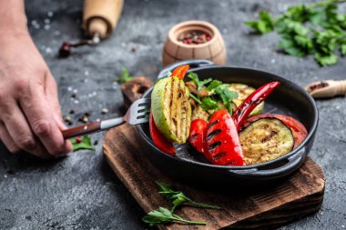 Dökme demir tavada servis edilen renkli ızgara sebzelerin cömertliği. Çeşitli barbekü vegan yemekleri..