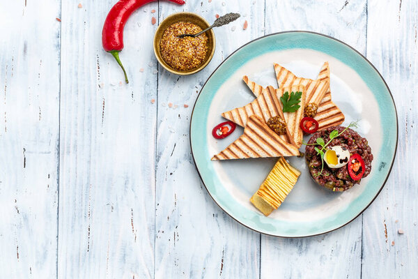 Beef tartare with capers, pickled cucumber and raw quail egg with bread toasts served on plate. French cuisine. banner, menu, recipe place for text, top view,