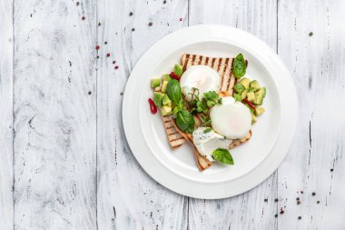 Kahvaltıda. Kızarmış ekmeğin üzerinde haşlanmış yumurta ve ahşap arka planda avokado tabağı. afiş, menü, metin için tarif yeri, üst görünüm.