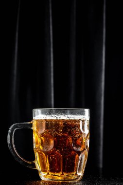Koyu arkaplanda bir kupa bira, kalın köpüklü cam, dikey görüntü. metin için yer.