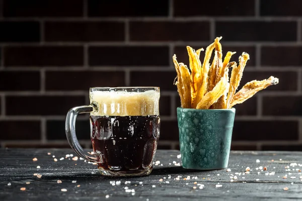 mug of beer on dark background, glass with thick foam, dried fish on wooden background. Beer brewery concept. Snack for beer dried smelts. Beer background.