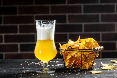 Cold beer glass with potato crisps on a bar counter with copy space.