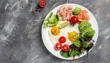 Ketojenik kahvaltı. Keto düşük karbonhidratlı somon, haşlanmış karides, karides, kızarmış yumurta, taze salata, domates, salatalık ve avokado. Üst görünüm.