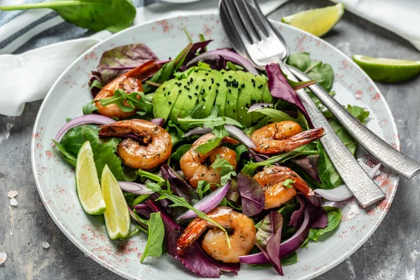 Green salad with avocado and shrimps salad. Seafood concept. Tasty veg mixed leaves, grilled prawn shrimps. Delicious breakfast or snack on a gray background, top view.