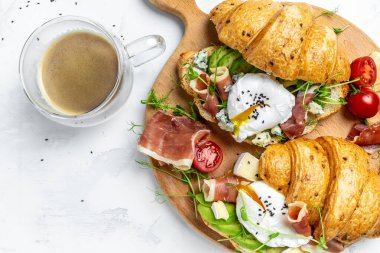 En iyi Benedict yumurtaları. Haşlanmış yumurtalı kruvasan sandviç, domates jambonu, jamon, mavi, peynir, ahşap tahtada avokado. Kahvaltı konsepti..