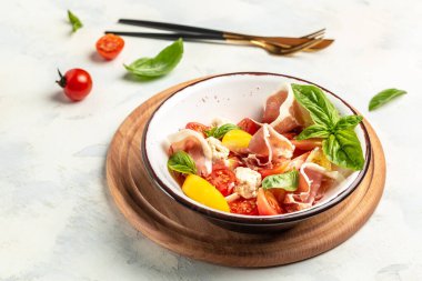 Domatesli, krem peynirli, jambonlu ve fesleğenli beyaz bir kâse taze ve sağlıklı Akdeniz salatası. Lezzetli dengeli gıda konsepti.