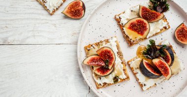 Taze incir, fesleğen yaprağı ve beyaz ahşap masada Philadelphia krem peynirli bruschetta..