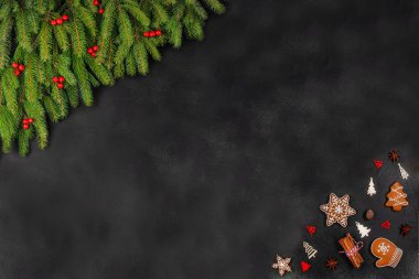 Noel arkaplanı köknar dalları, kırmızı böğürtlenler, zencefilli kurabiyeler ve koyu yüzeyde ahşap süslemeler, metin için metin alanı olan şenlikli düzlük