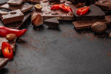 Fındık ve kırmızı biber dilimli çeşitli siyah ve sütlü çikolata parçaları koyu dokulu arka plan, baharatlı çikolata konsepti, üst görünüm kopyalama alanı.