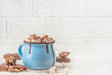 Bir fincan kremalı sıcak çikolata ve beyaz arka planda mavi bardakta kakao tozu, çikolata parçalı sıcak kış içeceği konsepti ve reklam tasarımı için fotokopi alanı.