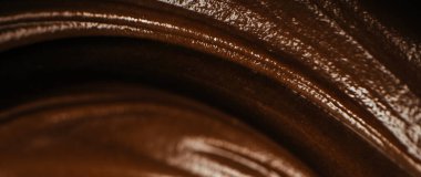 Erimiş siyah çikolatanın makro yakın çekimi parlak dokuları ve pürüzsüz kıvrımları tatlı tasarımı ve şekerleme konsepti için kremalı sıvı çikolatanın soyut arka planı