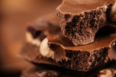 Close-up stacked chocolate pieces with crunchy texture and nuts on warm brown background for dessert branding and confectionery advertising