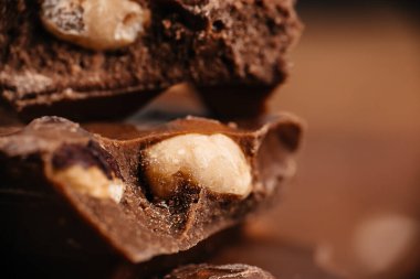 Macro view of broken chocolate pieces with whole nuts on a warm brown background ideal for dessert advertising and confectionery branding