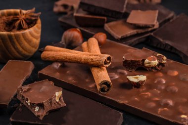 Assorted chocolate bars with nuts, cinnamon sticks and cocoa creating a rich gourmet dessert composition.