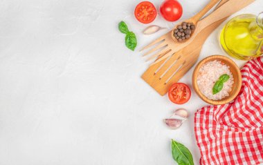 Top view of fresh cooking ingredients and kitchen utensils arranged on a white textured background. Tomatoes, basil, garlic, peppercorns, pink salt, olive oil
