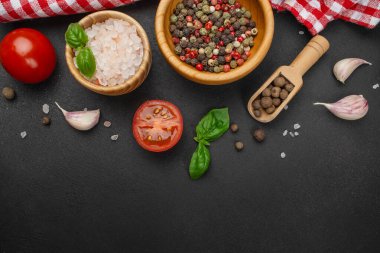 Top view of assorted fresh cooking ingredients arranged on a dark textured background, including tomatoes, garlic cloves, basil leaves, colorful peppercorns, and Himalayan salt in wooden bowls