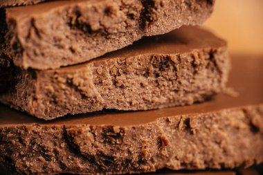 Katmanlı gözenekli sütlü çikolatanın katmanlı dokusu kaba hava yapısı ve sıcak ışıklandırması çerçeveyi dolduruyor, şekerleme reklamcılığı, ambalaj tasarımı ve tatlı yemek görselleri için ideal..