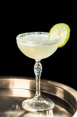 Siyah arka planda izole edilmiş tuzlu ve taze limon dilimli kristal coupe bardaktaki zarif margarita kokteyli, bar menüleri, içki markaları, kokteyl reklamları için mükemmel..