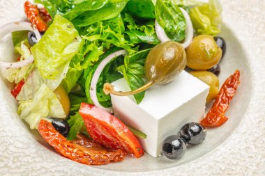 Feta peynirli, zeytinli, kapari üzümlü, güneşte kurutulmuş domatesli taze Yunan salatası ve yakın plan gevrek yeşillikler..