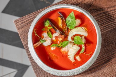 Karides, midye, beyaz balık ve taze fesleğenli gurme deniz ürünleri çorbası. Canlı domates suyunda servis ediliyor..