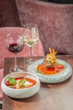 Modern bir restoranda, sörf ve güveç ile nefis bir yemek masası, deniz ürünleri çorbası ve bir bardak kırmızı ve beyaz şarap..