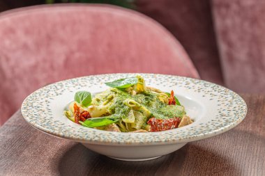 Süslü fesleğen soslu pappardelle makarna, tavuk parçaları, güneşte kurutulmuş domates ve çam fıstığı dekoratif bir kasede servis edilir..