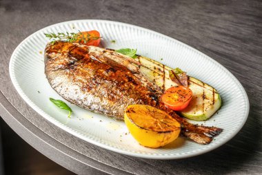 Kızarmış dorado balığı, kabak, kiraz domatesleri, şifalı otlar ve kızarmış limonla servis edilir.