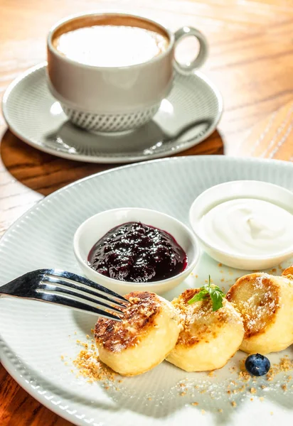 Bir fincan kahve, geleneksel kahvaltı ya da tatlı ile birlikte seramik tabakta çilek reçeli ve ekşi kremayla servis edilen kızarmış peynirli krep yakın plan.