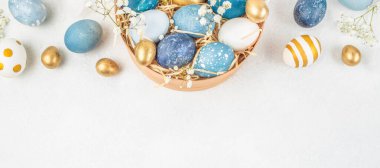 Süslü mavi, beyaz ve altın Paskalya yumurtaları ahşap kasede çiçekler ve samanla, üst görünüm düz beyaz zemin üzerinde uzanır metin için büyük kopya alanı ile