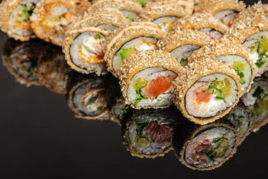 Kızarmış suşi rulolarını somon, karides, krem peynir ve salatalıkla kapatın. Koyu düşünceli arka planda, restoran menüsü, yemek teslimatı, reklam ve afiş tasarımı için mükemmel.