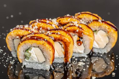 Koyu arkaplanda yılan balığı soslu, mango soslu, krem peynirli ve pirinçli fırınlanmış suşi rulosu, restoran menüsü, yemek teslimatı, reklam ve pankart tasarımı için ideal Japon füzyon mutfağı..