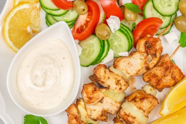 Taze salatalık ve domates salatasıyla servis edilen sulu ızgara tavuk şişleri, zeytin, limon ve krema sosu beyaz tabakta, üst manzara besin bileşimi