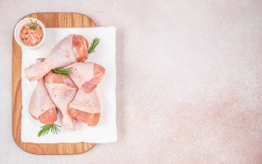 Beyaz tabağa yerleştirilmiş çiğ tavuk budu ve ahşap tahtada biberiye ve pembe tuz. Arka planda ışık desenli fotokopi alanı, üst görünüm.