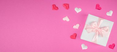 Pembe kurdeleli beyaz hediye kutusu pembe arka planda dekoratif kalplerle çevrili, romantik konsept, üst görünüm, kopyalama alanı