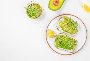 Krem peynirli, mikroyeşillikli ve limonlu sağlıklı avokado tostunun en üst görüntüsü geniş bir kopya alanına sahip beyaz arka planda, temiz yemek, kahvaltı, vegan diyeti, yemek blogları, reklamcılık ve menü tasarımı için ideal