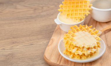 Altın ev yapımı waffle 'lar ahşap bir tahtanın üzerine konulmuş süt sosuyla servis ediliyor. Fotokopi alanı olan ahşap masa arkaplanı üzerinde. Kahvaltı menüleri, tatlı reklamları, yemek blogları ve kafe tasarımı için mükemmel.