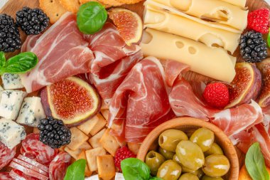 Prosciutto, dilimlenmiş peynir, mavi peynir, incir, zeytin, kraker ve taze böğürtlenli ahşap tahta, üst manzara, gurme aperatifi ve parti yemeği konsepti.