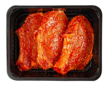 Baharatlı domuz bifteği, siyah plastik tepside terbiye edilmiş taze et hazırlama konsepti, beyaz arka planda izole edilmiş.